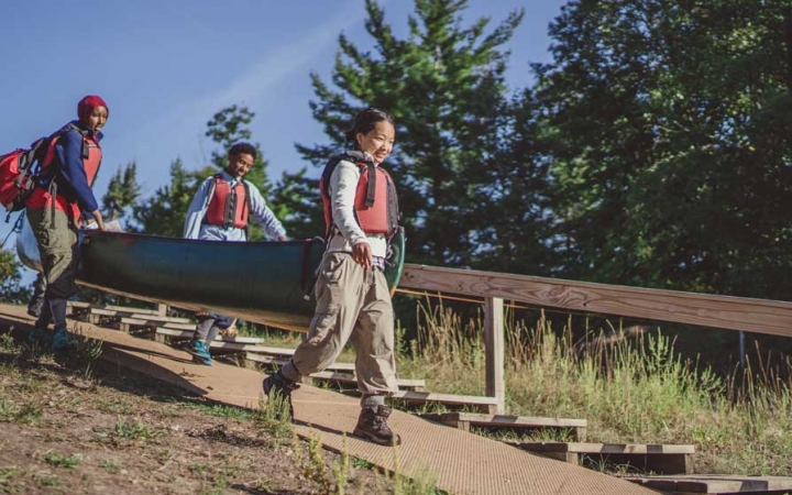 young teens carry a canoe to the water on outdoor course